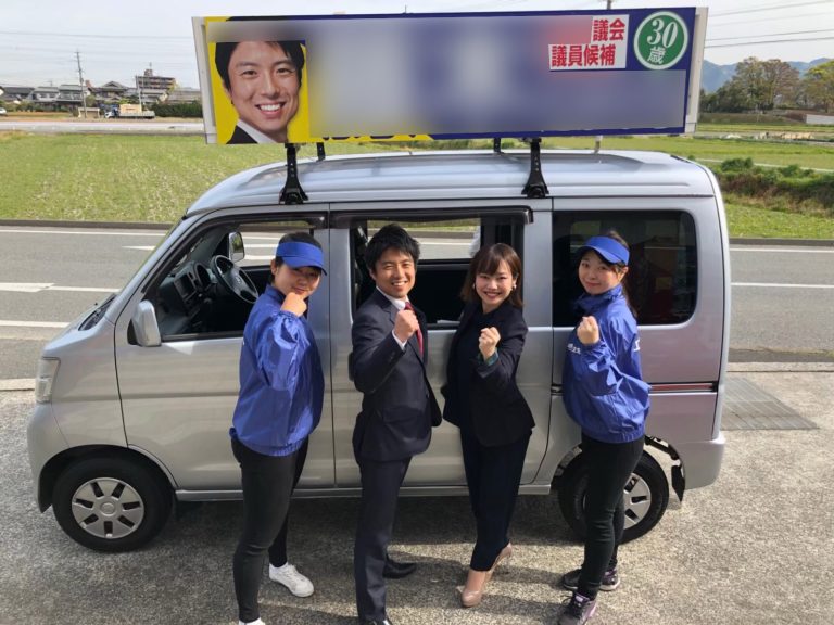 2019年地方議会議員選挙戦で選挙カーの前でガッツポーズする候補とウグイス