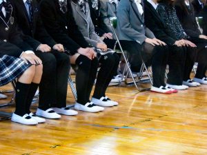 学生が講堂でパイプ椅子に座る画像
