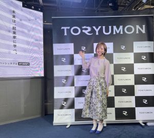 TORYUMONのパネル前でポーズをとるMCの平野綾菜