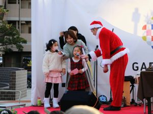 ステージの上に子供２人とMCの女性、サンタの男性