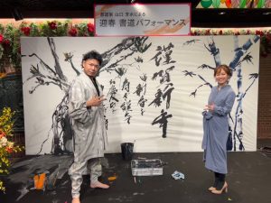 迎春書道パフォーマンスのステージ上に書道家とMC女性