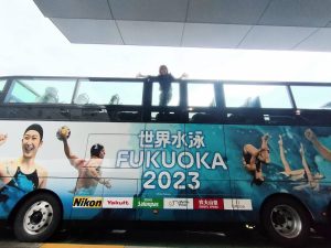 世界水泳FUKUOKA2023仕様のオープントップバスの上に女性