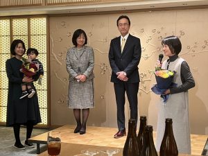 壇上に男女とその下に花束を持つ女性と子供を抱える女性