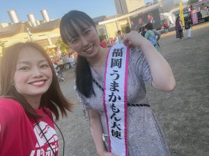 福岡うまかもん大使のたすきをかけた女性とリポーターの女性