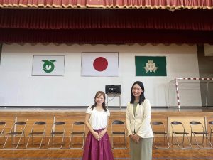 体育館のステージ前に並べらた椅子の前に立つ女性2人