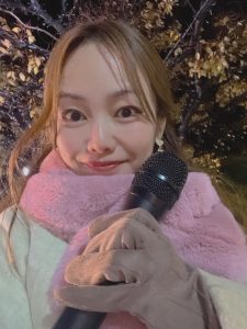 夜、マフラーをしてマイクを持つ女性