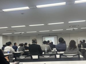 長テーブルに座り説明を聞く大勢の人