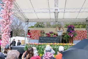 ステージ上で両手をあげる男性と司会の女性