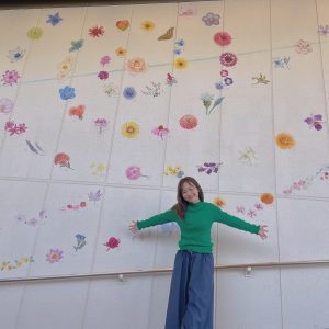花の絵が描かれた壁の前に女性