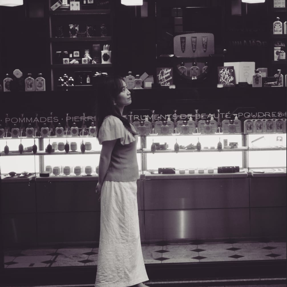福岡のアナウンサー・司会者 平野綾菜が、パリの香水店で横向きに立ち、上を見上げている様子(モノクロ写真)