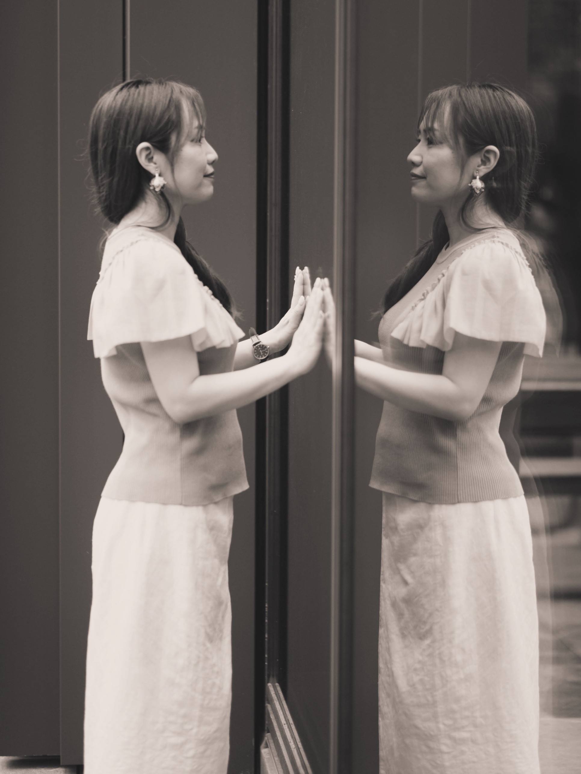 福岡のアナウンサー・司会者 平野綾菜が、鏡に映った自分と手を合わせている様子(モノクロ写真)