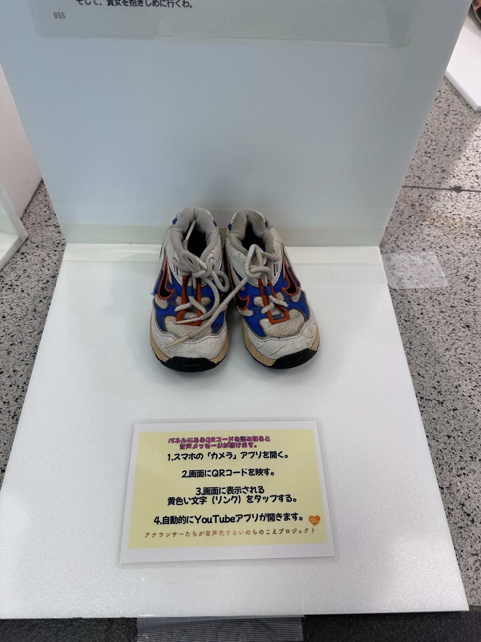 生命のメッセージ展で展示されているメッセンジャーの靴。QRコードを読み取ると音声メッセージが聴ける案内が添えられている(福岡市役所会場)