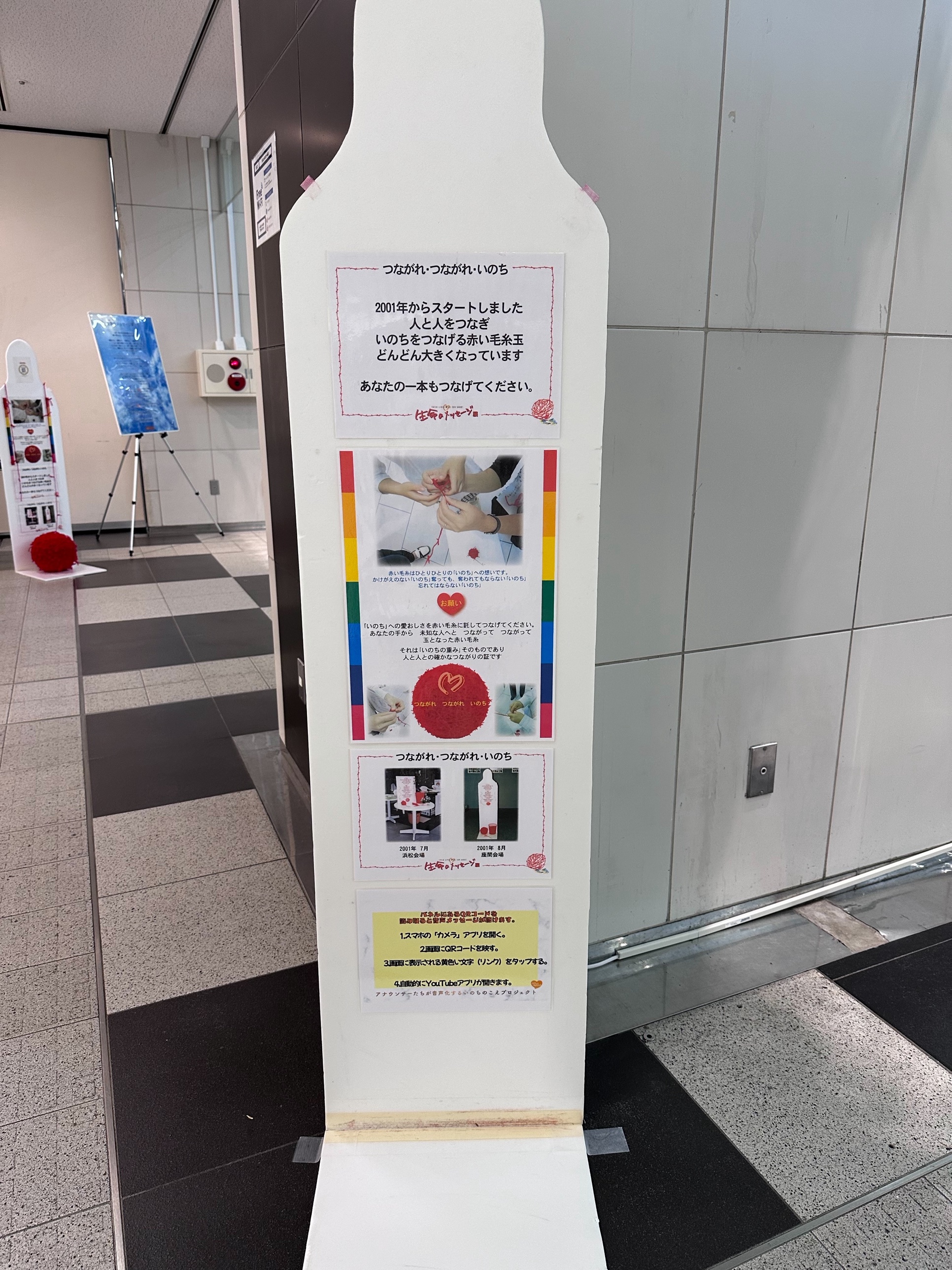 「つながれ・つながれ・いのち」赤い毛糸玉プロジェクトの案内。2001年から続く、人と人をつなぎ命をつなげる取り組みで、来場者が赤い毛糸を結んでいく