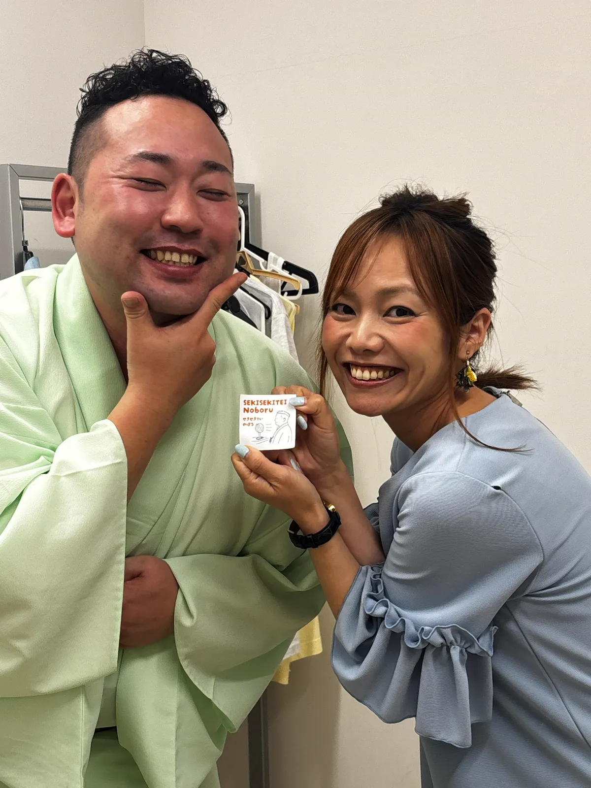 楽屋で、落語家の昔昔亭昇さんと平野綾菜が笑顔で並ぶ。平野が昇さんのイラスト入りのカードを手にしている