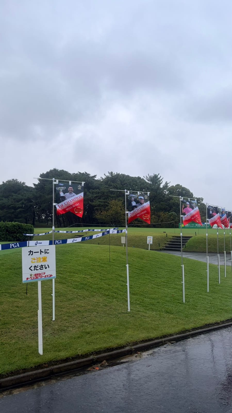 今年の大会。雨の福岡カンツリー倶楽部 和白コースに歴代優勝者のバナーが並び、手前に「カートにご注意ください」の看板
